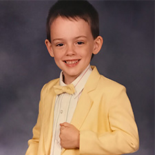 A young boy in a pastel yellow suit jacket and bowtie smiles at the camera.