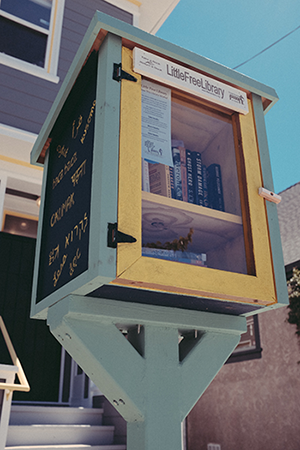 A wooden box in front of a house that serves as a small free library for folks around the neighborhood.