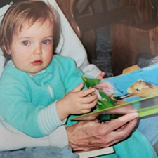 A toddler wearing a teal sleep suit turns the pages of a book.
