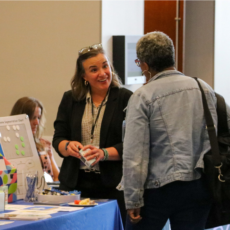 A summit exhibitor speaks with a summit attendee at her exhibit table.