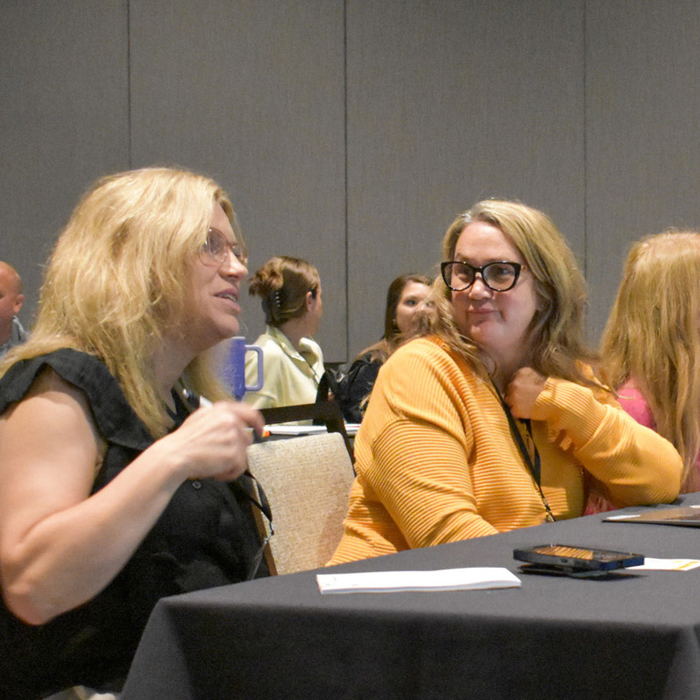 Two teachers sit at a table and talk.