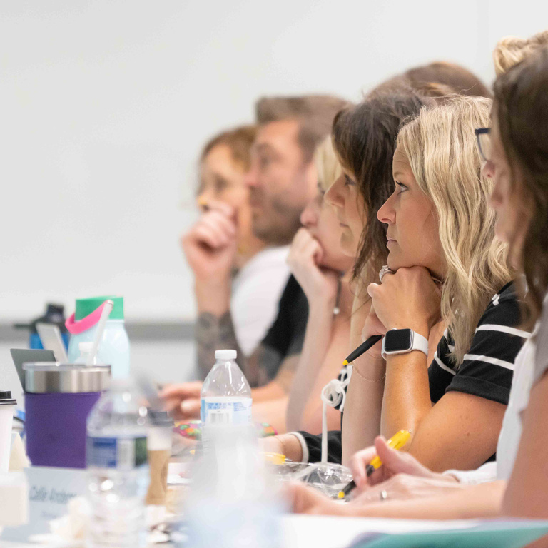 School administrators sit at a desk taking notes and watching a presenter