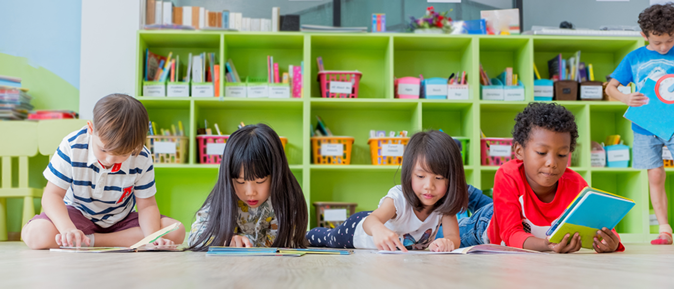 four children reading on floor by classroom library