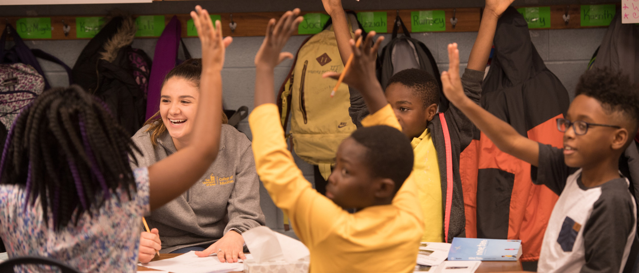 College of Education student smiles at elementary schoolers raising their hands