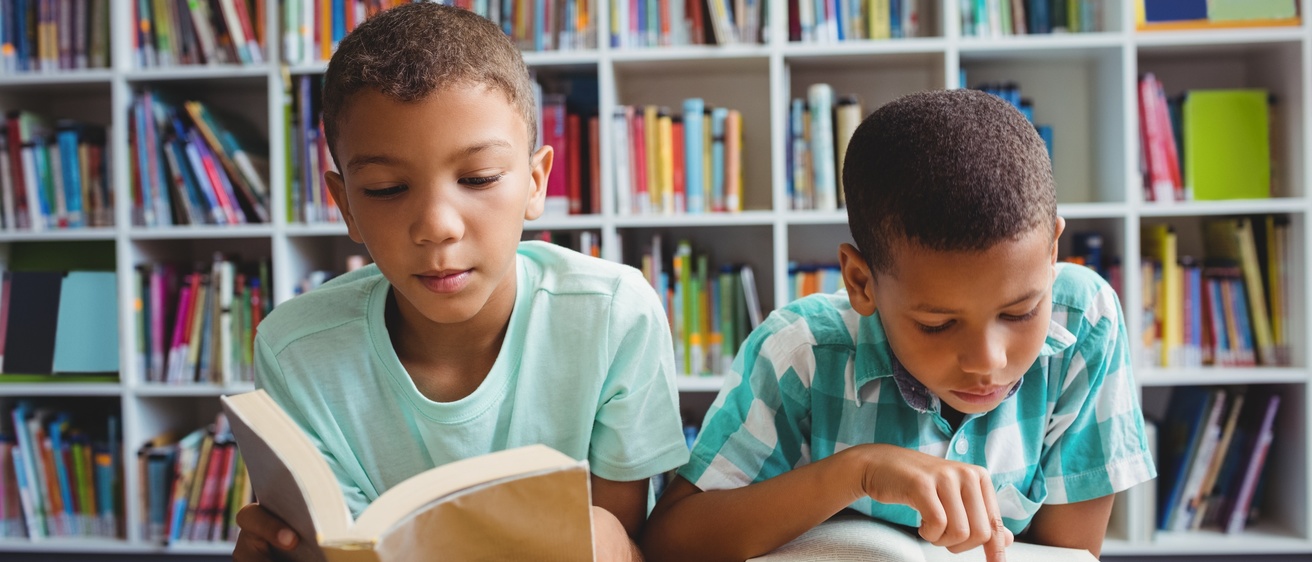 Two young boys read books in a library
