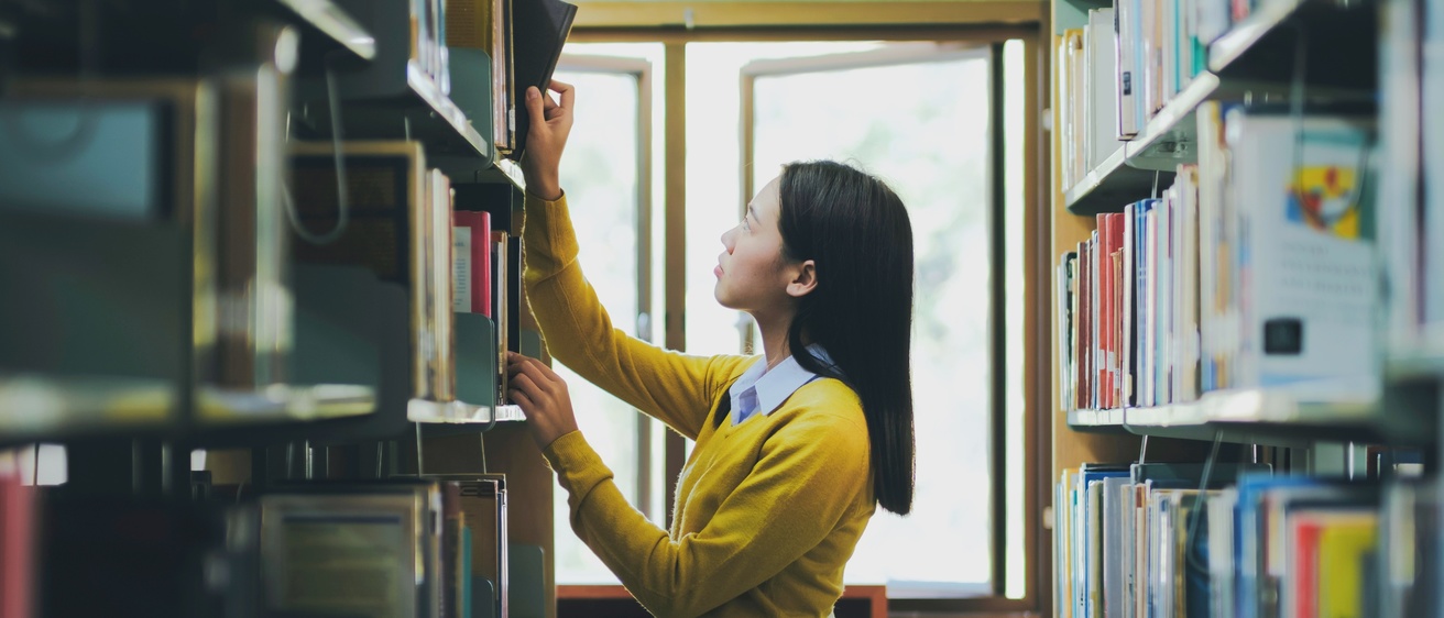 A student looks for a book on a row of shelves in a library