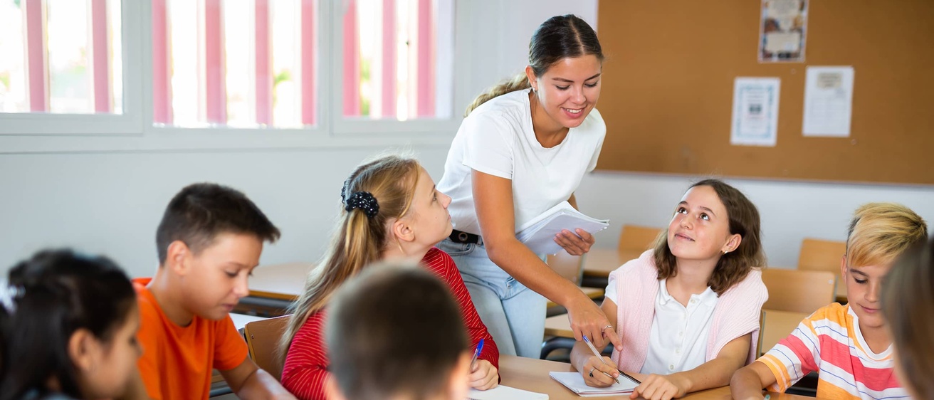 A teacher leans over a table to help a group of students