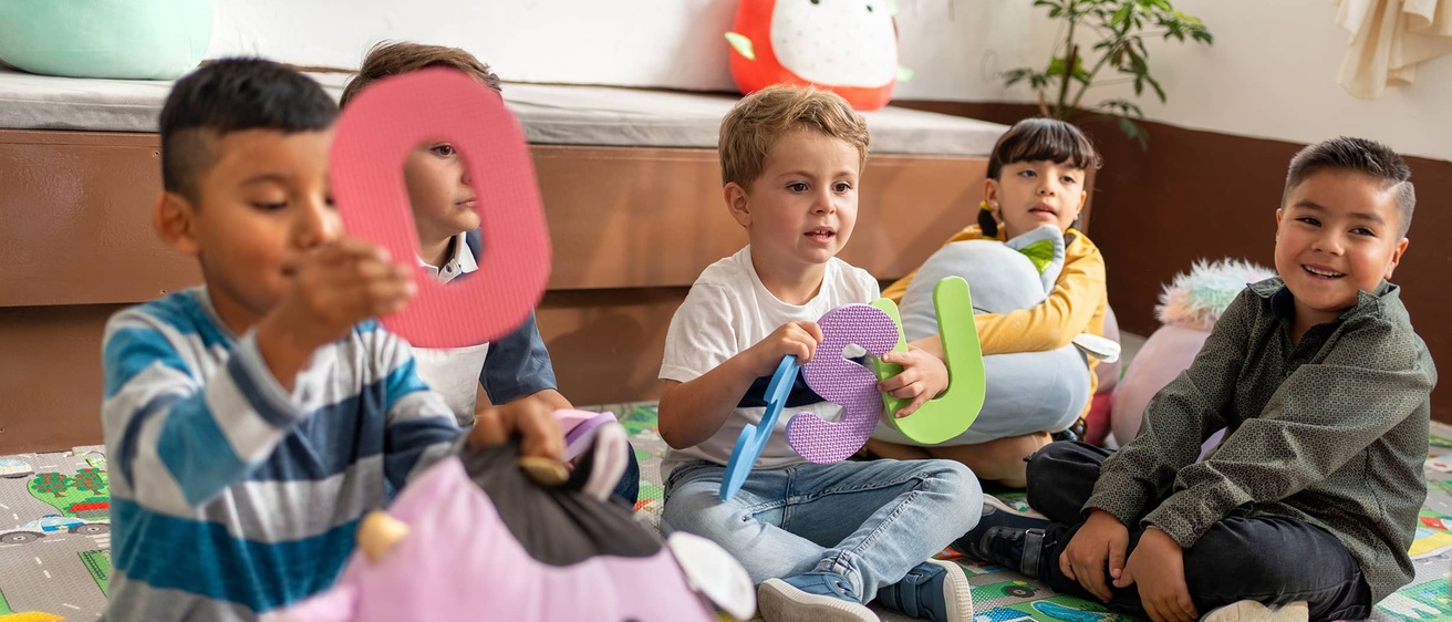 Preschool students hold up foam letters of the alphabet