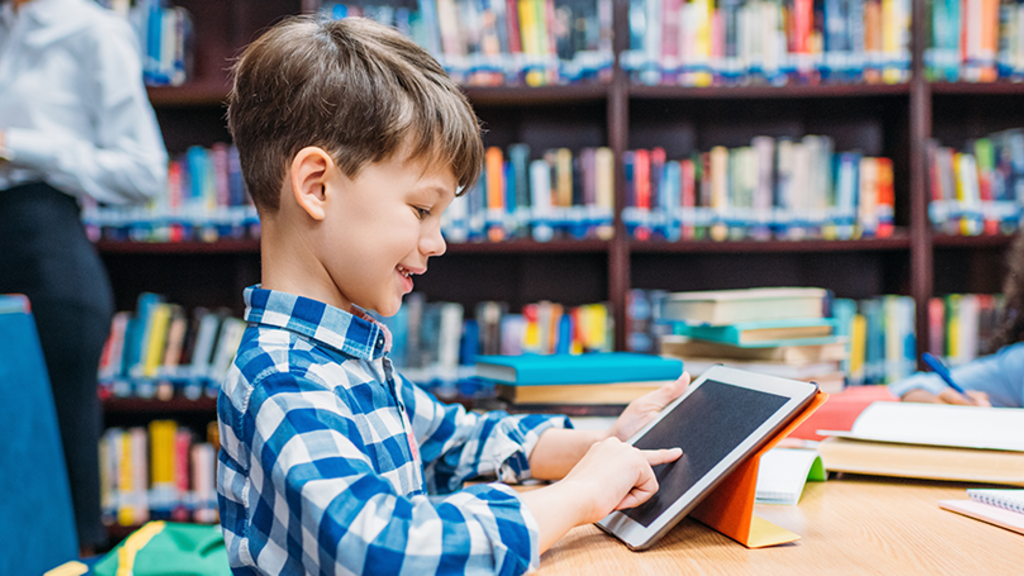 Young boy with brown hair uses a tablet to read at a library table