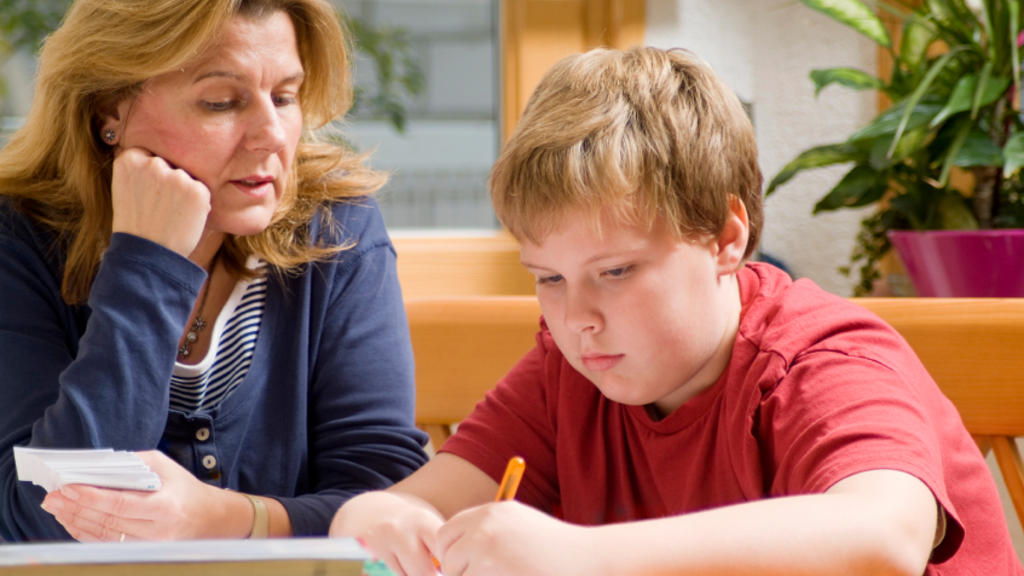 Child writing out a graphic organizer at a desk with his mother's help