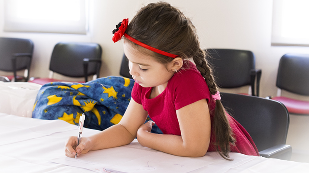 Young girl in red clothes writing on a piece of paper on a desk