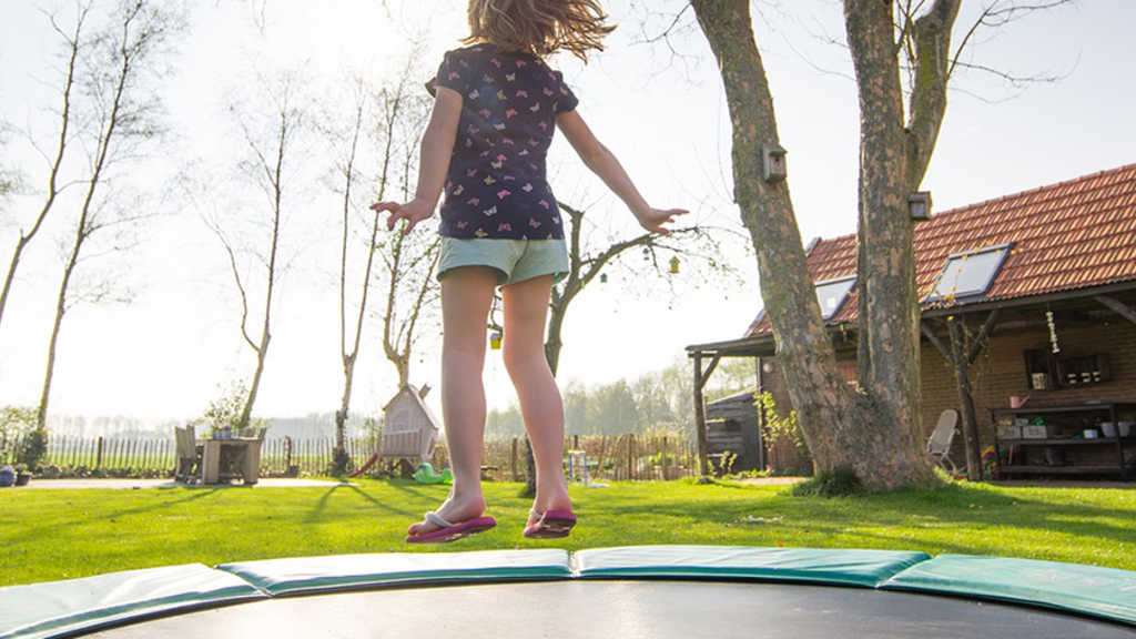 A girl jumps on a trampoline in a backyard with clear, warm weather.