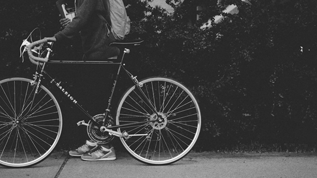Black and white image of a student walking with their bike on the sidewalk