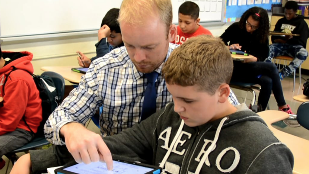 A teacher helps a student with literacy work on a tablet