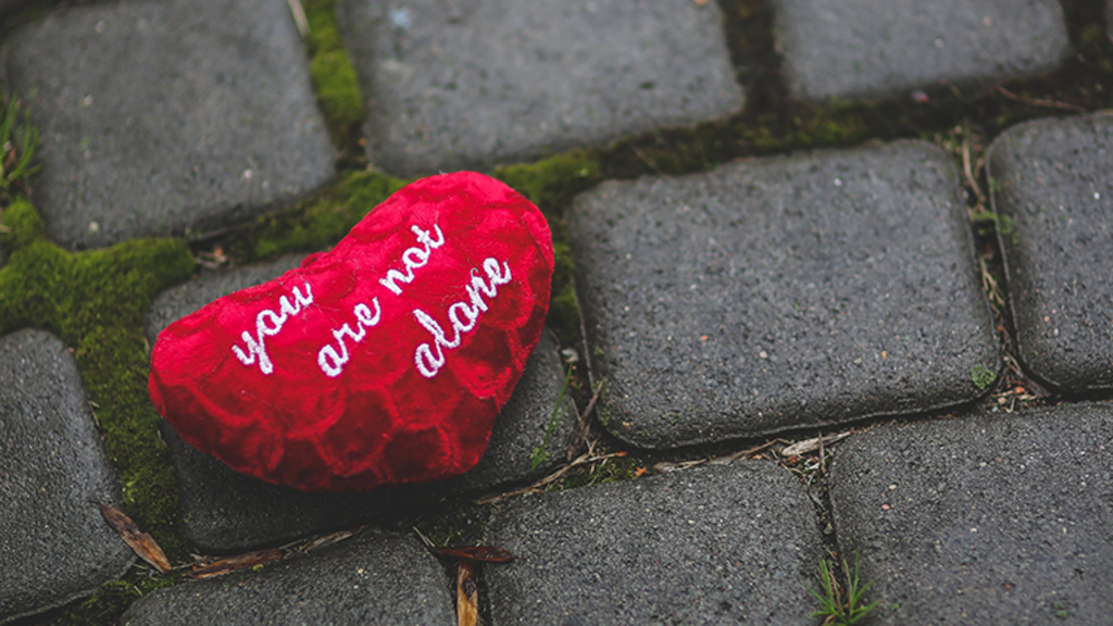 A heart on the sidewalk with embroidered white letters saying "you are not alone"
