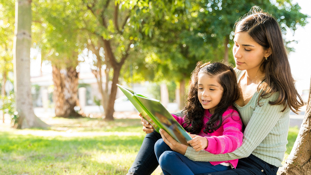 girl reads in her mother's lap