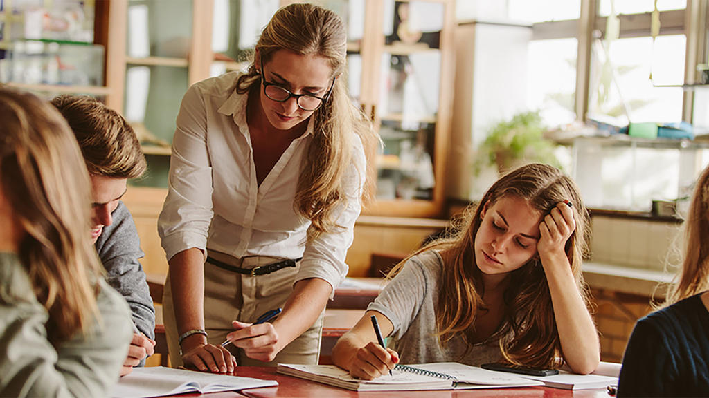 teacher leans over student's desk