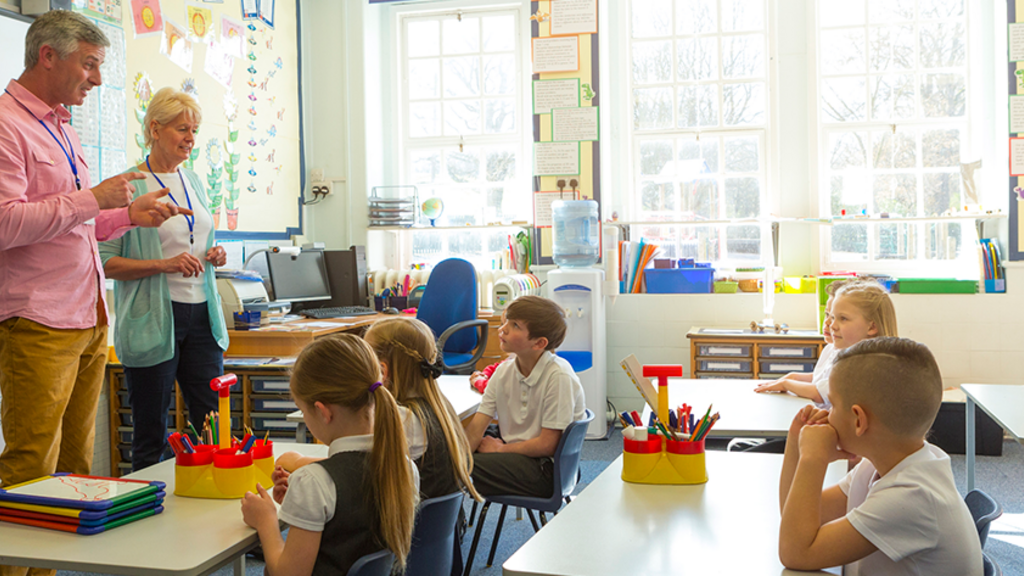two teachers stand at the front of a classroom