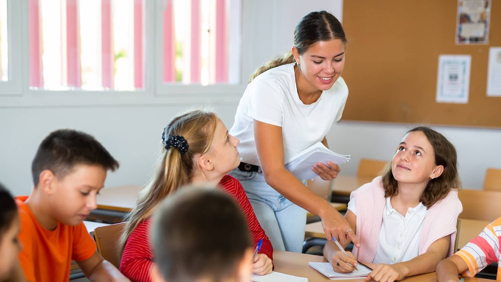 A teacher leans over a table to help a group of students