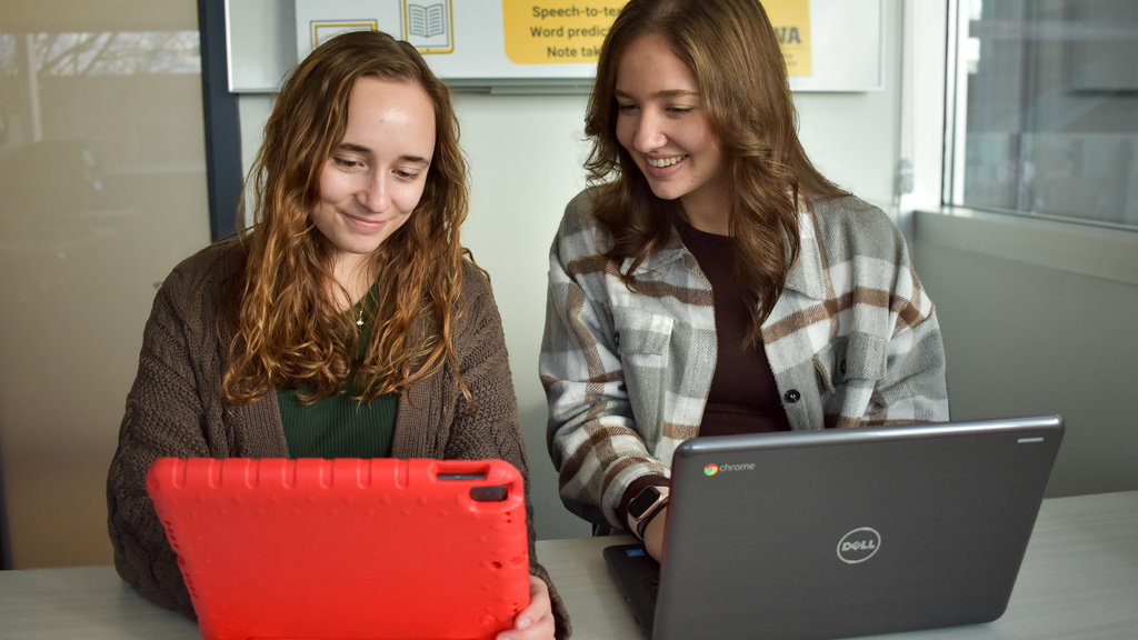 Two assistive technology coordinators work on an iPad and a laptop.